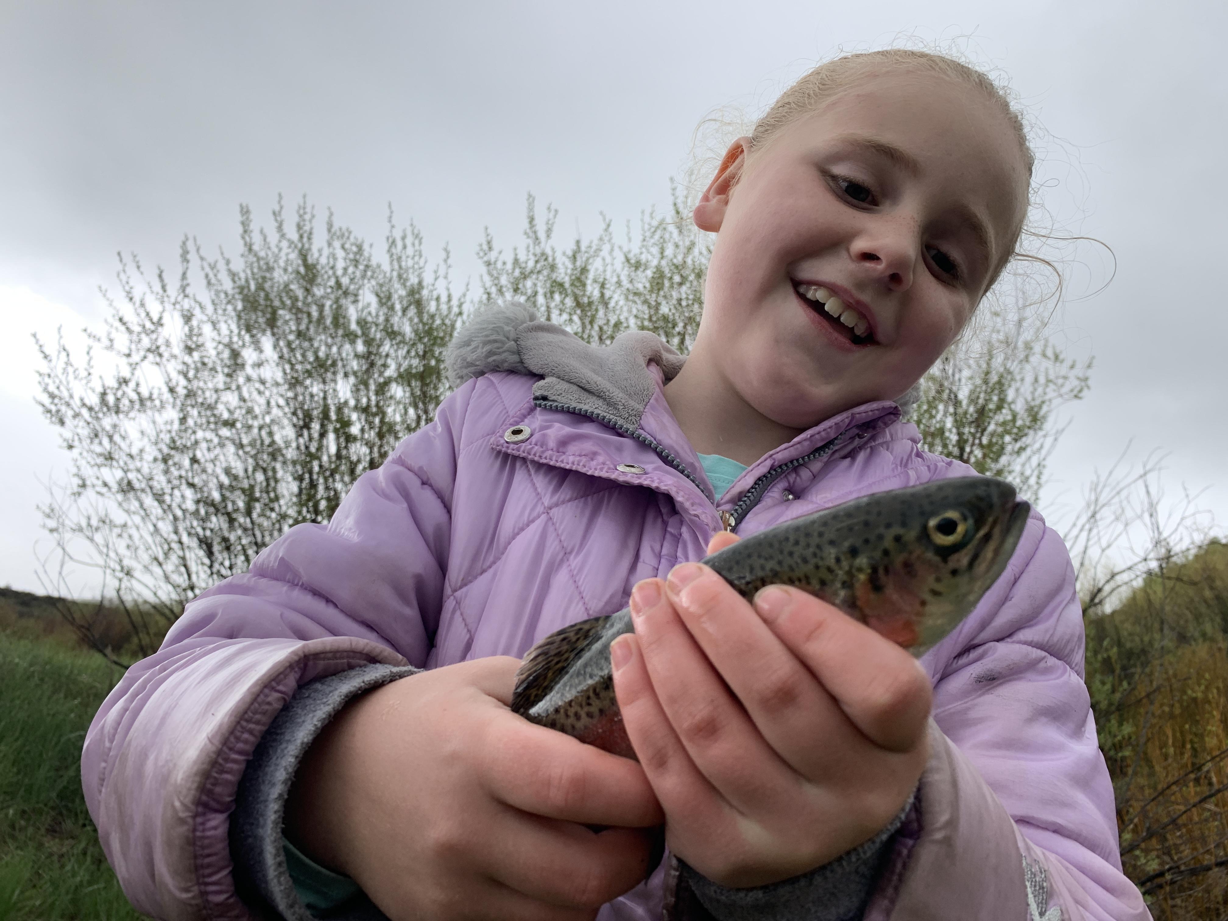 Little girl holding a rainbow trout and smiling